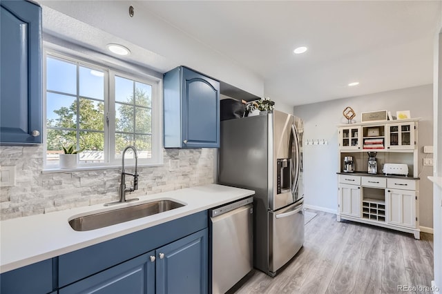 kitchen with backsplash, stainless steel appliances, sink, blue cabinetry, and light hardwood / wood-style flooring