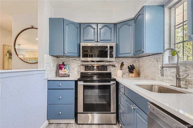 kitchen featuring decorative backsplash, stainless steel appliances, blue cabinetry, and sink