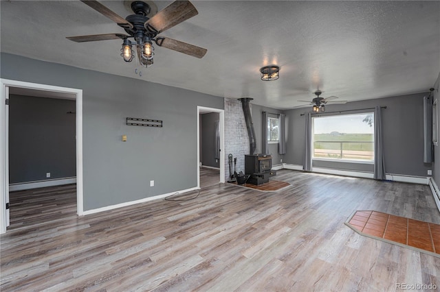 9940 N Calhan Hwy, Calhan, CO 80808 - unfurnished living room featuring ceiling fan, a wood stove, wood finished floors, a baseboard radiator, and a textured ceiling