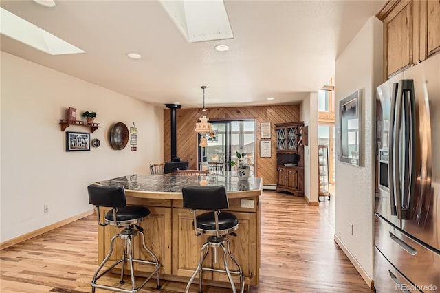 10450 Hondah Dr, Littleton, CO 80127 - kitchen featuring stainless steel fridge, a skylight, a breakfast bar area, a wood stove, and light wood-type flooring