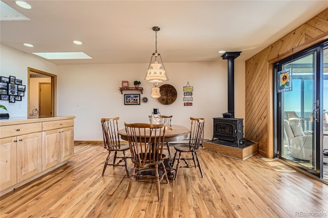 10450 Hondah Dr, Littleton, CO 80127 - dining area with a skylight, a wood stove, light wood-style flooring, wood walls, and baseboards