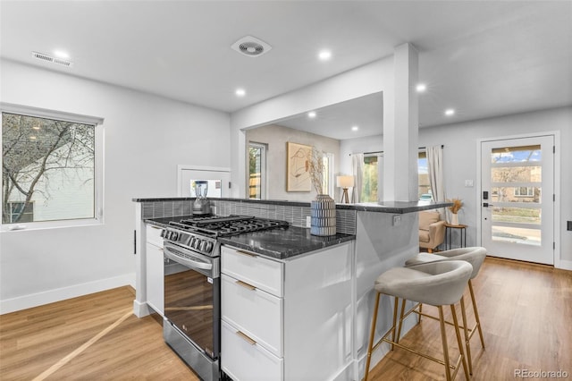 1220 Ash St, Denver, CO 80220 - kitchen with light wood finished floors, a kitchen bar, stainless steel range with gas stovetop, white cabinets, and visible vents
