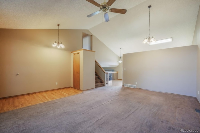 unfurnished living room with ceiling fan with notable chandelier, high vaulted ceiling, and carpet flooring