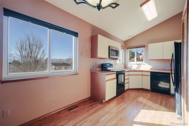 kitchen featuring sink, white cabinetry, vaulted ceiling, light hardwood / wood-style flooring, and black appliances