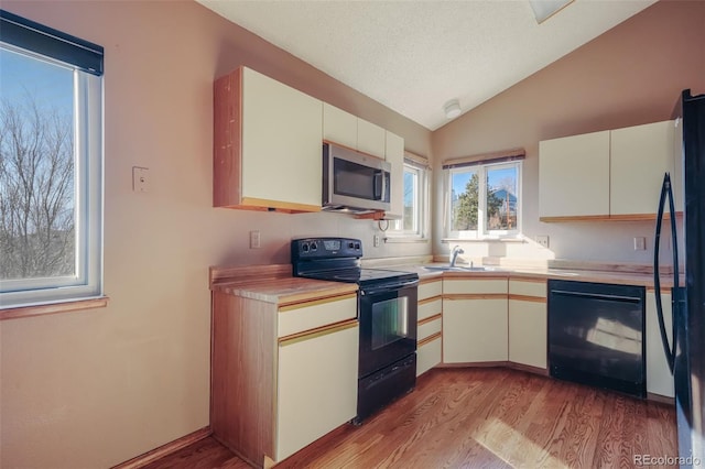 kitchen with lofted ceiling, sink, black appliances, and light wood-type flooring