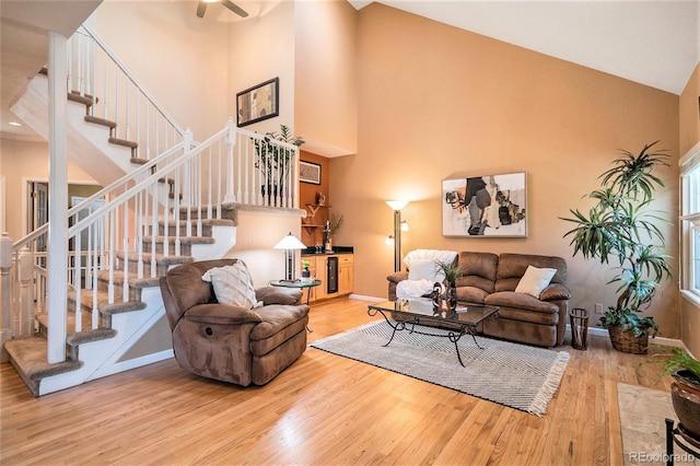 living room featuring wood finished floors, stairway, high vaulted ceiling, baseboards, and a ceiling fan
