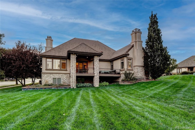 back of house featuring stone siding, a chimney, a lawn, and stucco siding