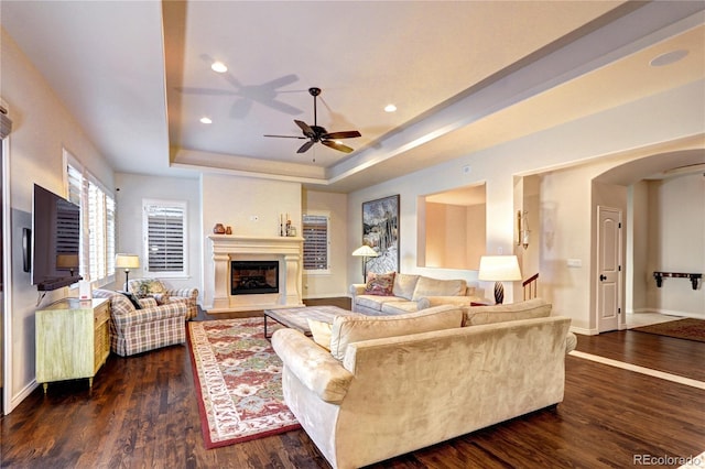 living area with arched walkways, dark wood finished floors, recessed lighting, a raised ceiling, and a glass covered fireplace