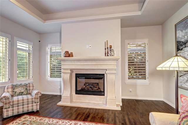 living area with a tray ceiling, a glass covered fireplace, and dark wood finished floors