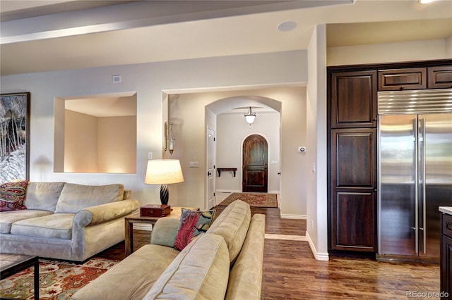 living area featuring arched walkways, dark wood finished floors, and baseboards