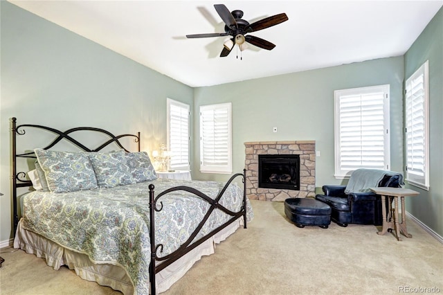 bedroom with light carpet, a fireplace, baseboards, and ceiling fan