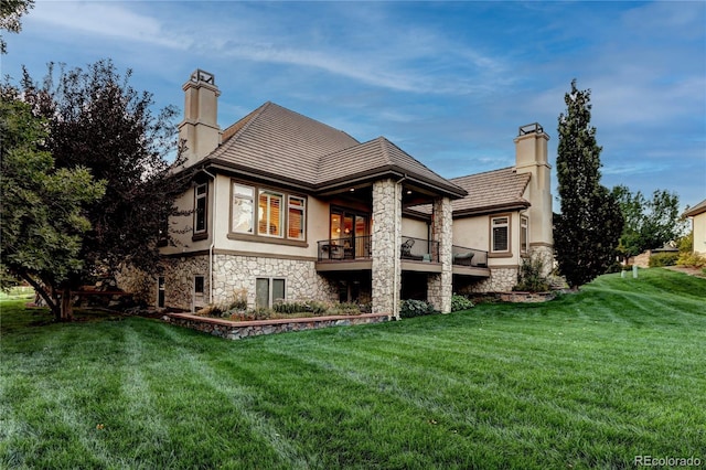 back of house featuring stone siding, a chimney, a lawn, and stucco siding