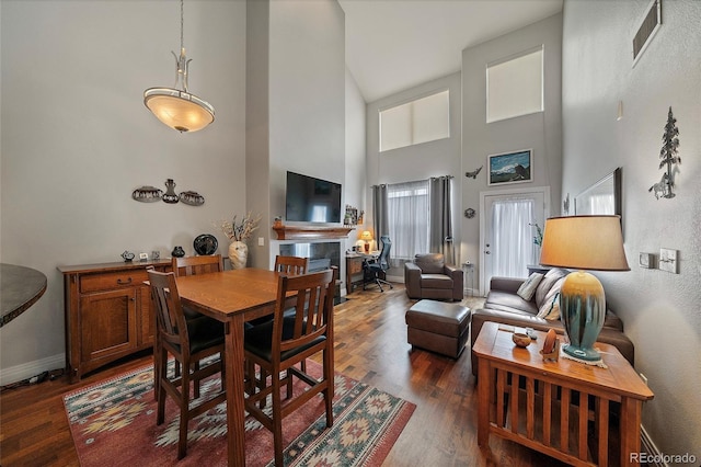 dining space with dark wood-type flooring, a high ceiling, visible vents, baseboards, and a tiled fireplace