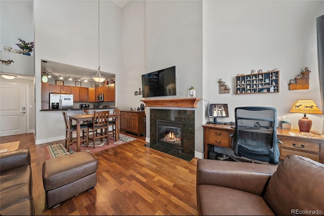 living room featuring a fireplace, a towering ceiling, baseboards, and wood finished floors