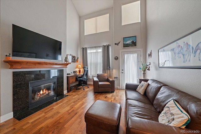 living room featuring light wood-type flooring, a fireplace, a towering ceiling, and baseboards