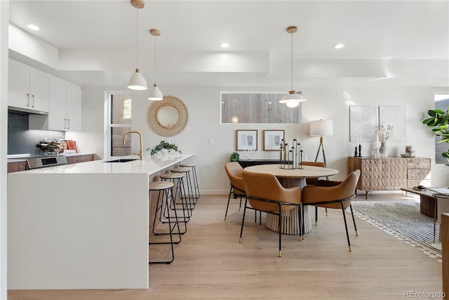 kitchen with a breakfast bar, light countertops, light wood-type flooring, white cabinetry, and a sink