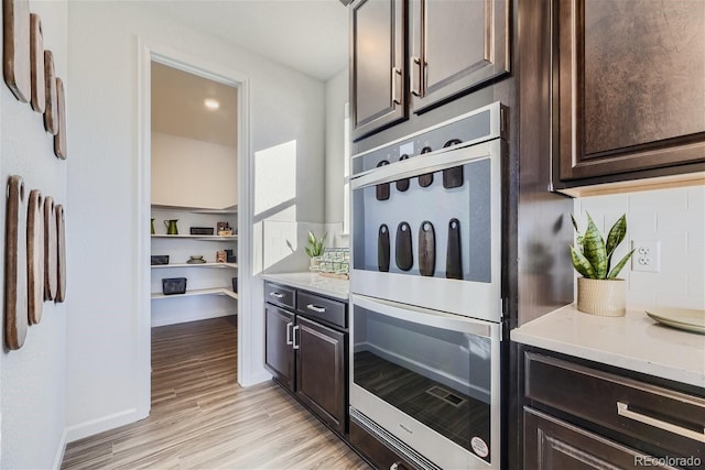 kitchen with light wood-type flooring, open shelves, double oven, dark brown cabinetry, and decorative backsplash