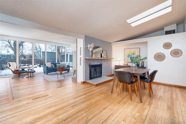 dining space featuring hardwood / wood-style flooring, lofted ceiling with skylight, a brick fireplace, and a textured ceiling