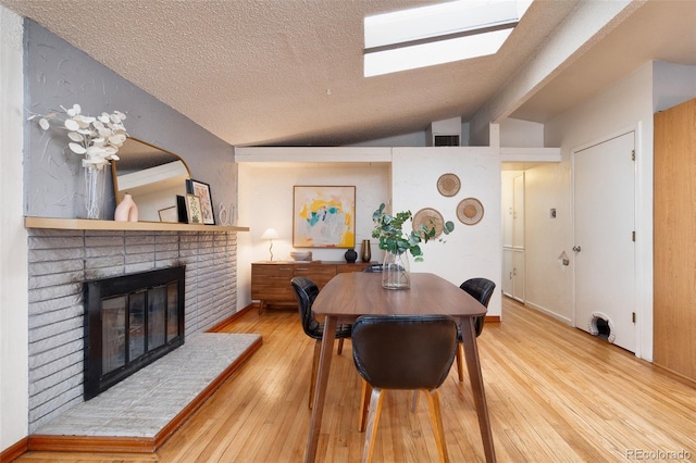 dining room with hardwood / wood-style flooring, lofted ceiling with skylight, a textured ceiling, and a fireplace