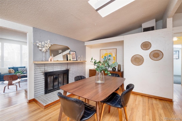 dining space featuring hardwood / wood-style floors, vaulted ceiling with skylight, a textured ceiling, and a fireplace