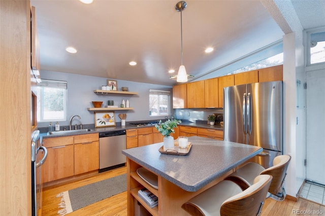 kitchen featuring sink, vaulted ceiling, appliances with stainless steel finishes, a kitchen island, and light hardwood / wood-style floors