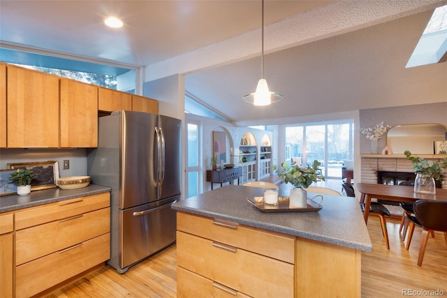 kitchen with a kitchen island, pendant lighting, stainless steel refrigerator, vaulted ceiling with beams, and light hardwood / wood-style floors