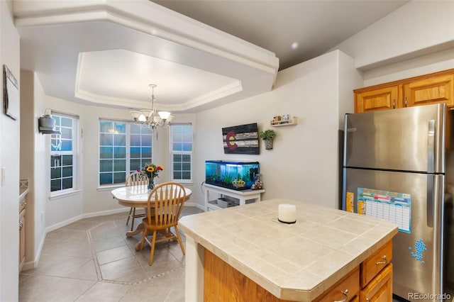 kitchen featuring brown cabinets, a tray ceiling, freestanding refrigerator, tile counters, and a chandelier