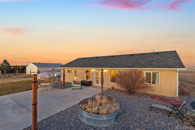 back of property at dusk featuring stucco siding, a patio, and a shingled roof