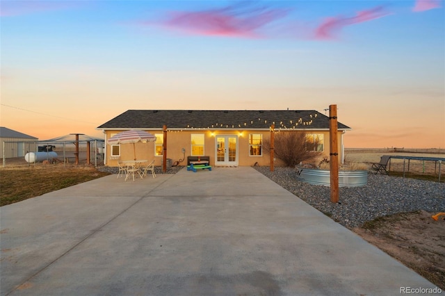 back of house at dusk with french doors, a patio, fence, and stucco siding