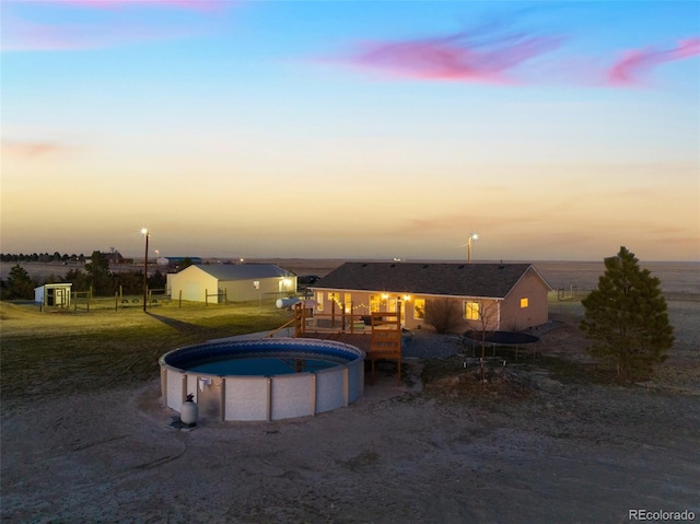 pool at dusk with an outdoor pool and a yard