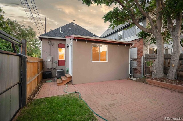 rear view of house with stucco siding, a patio, central AC, a fenced backyard, and roof with shingles