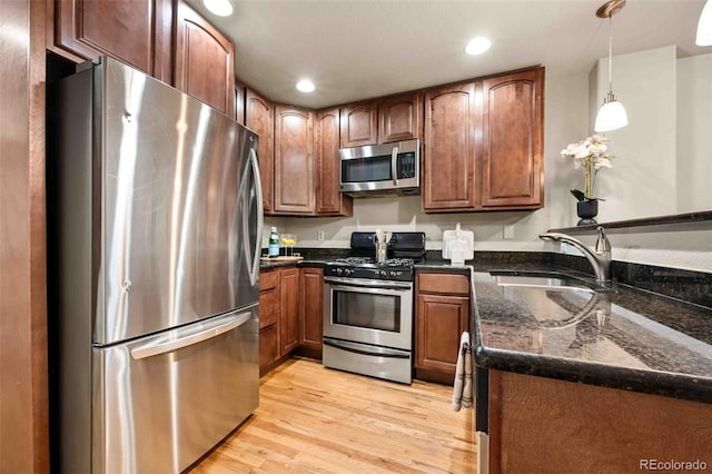 kitchen with sink, dark stone counters, light wood-type flooring, pendant lighting, and stainless steel appliances