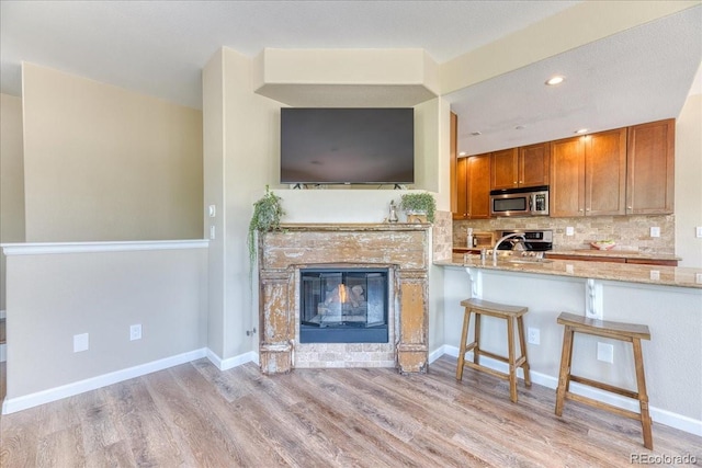 31112 Black Eagle Dr Unit 101, Evergreen, CO 80439 - kitchen featuring stainless steel microwave, brown cabinets, light wood-style flooring, light stone counters, and tasteful backsplash