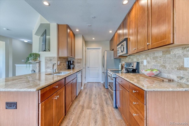31112 Black Eagle Dr Unit 101, Evergreen, CO 80439 - kitchen featuring appliances with stainless steel finishes, light wood-style flooring, light stone countertops, a peninsula, and decorative backsplash
