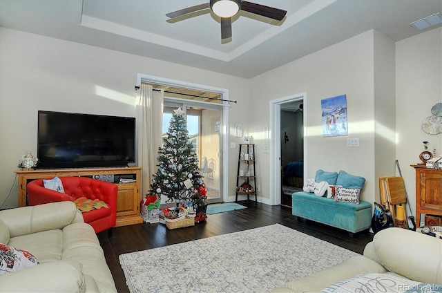 living room featuring dark wood finished floors, visible vents, ceiling fan, and a tray ceiling