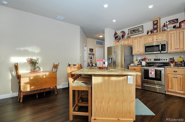 kitchen featuring a breakfast bar, an island with sink, stainless steel appliances, light stone countertops, and dark wood-type flooring