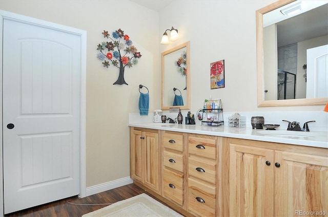 full bathroom featuring a shower with shower door, a sink, wood finished floors, double vanity, and baseboards