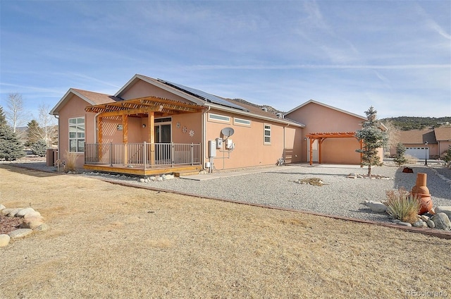 view of front facade featuring stucco siding, roof mounted solar panels, driveway, and a pergola