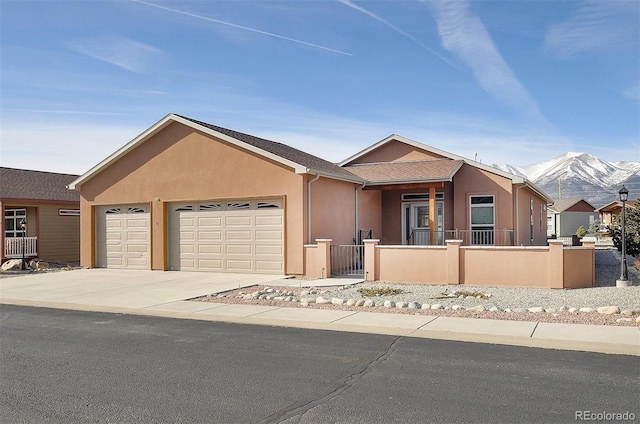 ranch-style home featuring an attached garage, stucco siding, concrete driveway, a fenced front yard, and a mountain view