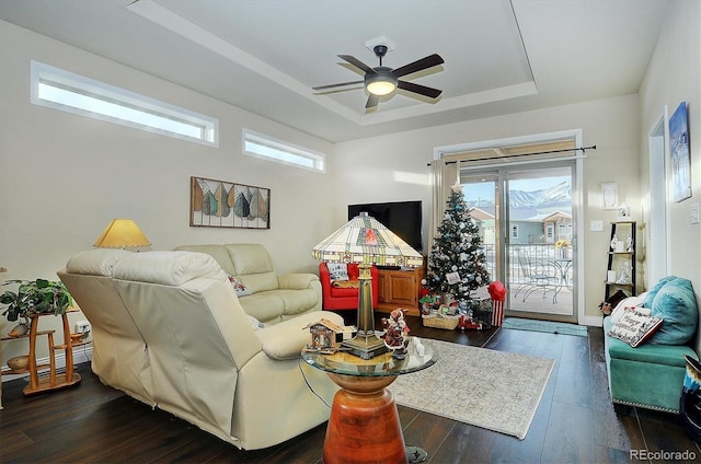 living room with dark wood-style floors, a raised ceiling, and a ceiling fan