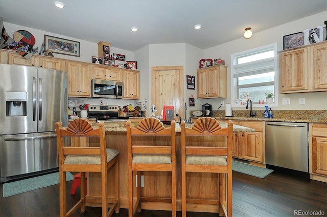 kitchen with a breakfast bar, light brown cabinets, dark wood finished floors, stainless steel appliances, and light stone countertops