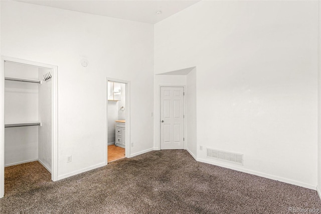 unfurnished bedroom featuring carpet, baseboards, a high ceiling, a closet, and ensuite bathroom