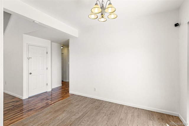 empty room featuring wood finished floors, a chandelier, and baseboards