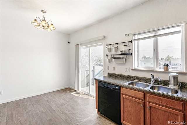 kitchen featuring dishwasher, a sink, dark countertops, light wood finished floors, and a chandelier