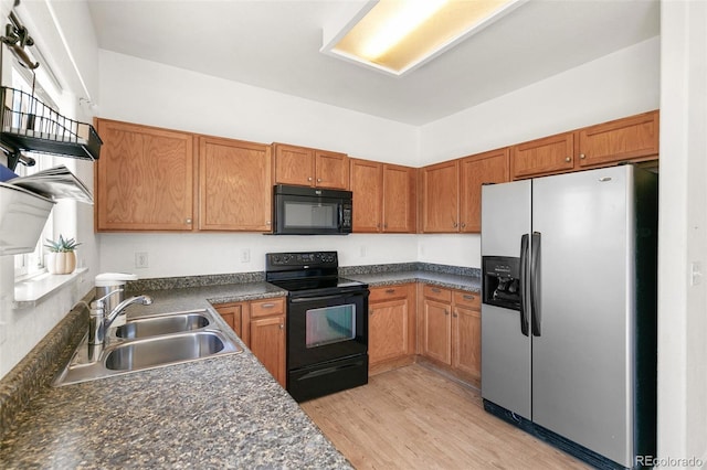 kitchen featuring black appliances, a sink, dark countertops, light wood-type flooring, and brown cabinets