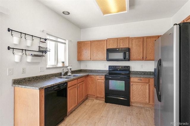 kitchen with black appliances, a sink, light wood finished floors, and dark countertops