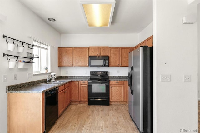kitchen featuring black appliances, a sink, dark countertops, light wood-style floors, and brown cabinets
