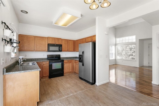 kitchen with black appliances, a sink, light wood-type flooring, dark countertops, and brown cabinets