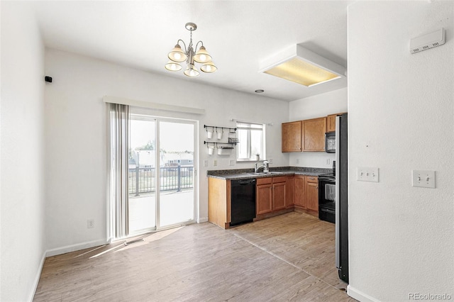 kitchen with black appliances, brown cabinetry, light wood finished floors, dark countertops, and a chandelier