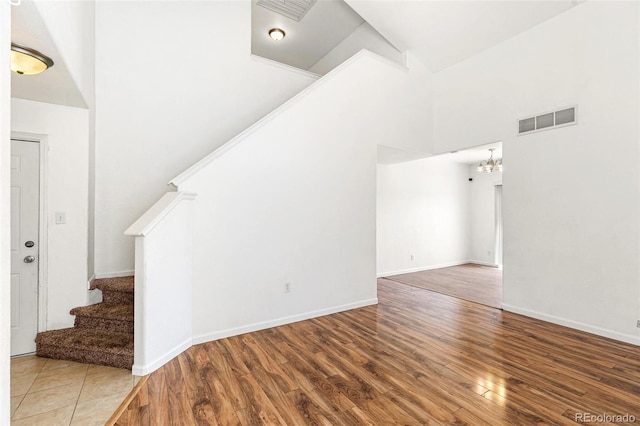unfurnished living room featuring stairway, wood finished floors, a high ceiling, a chandelier, and baseboards